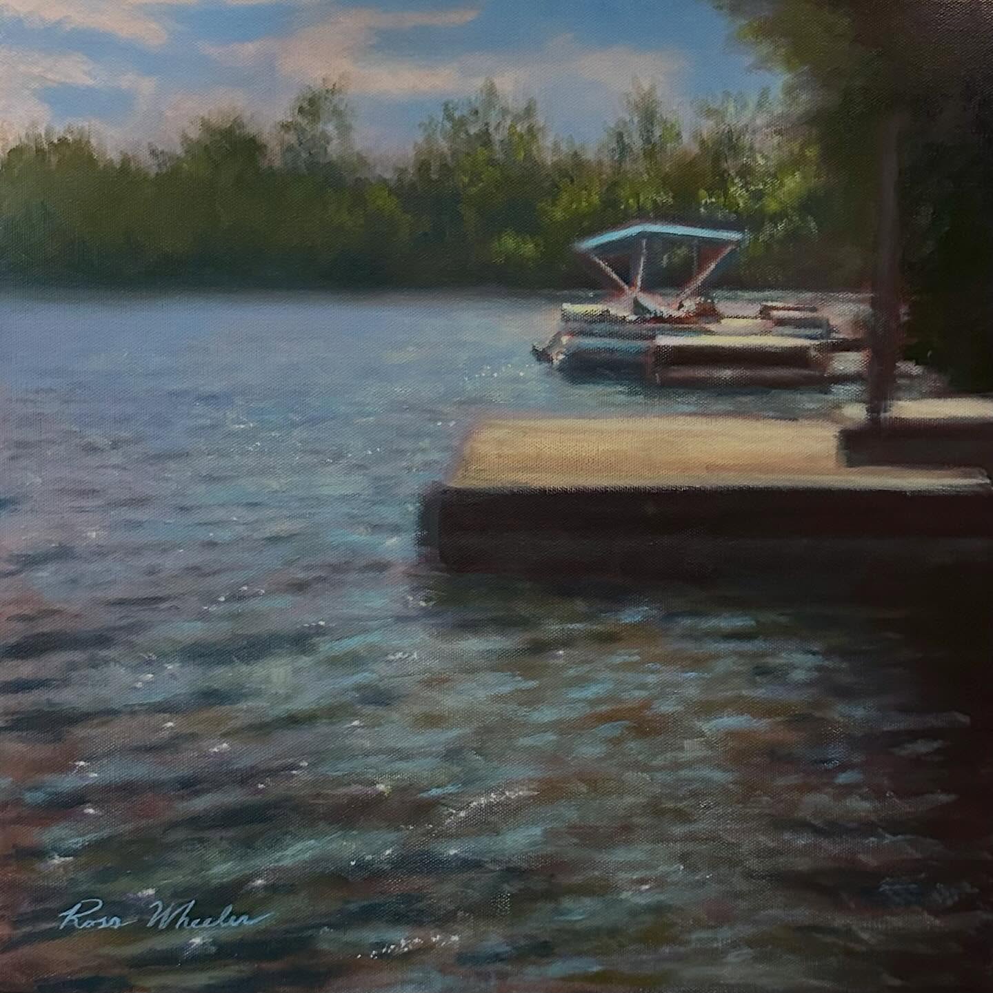 Plein air oil painting of a dock and boat on a calm lake with reflections